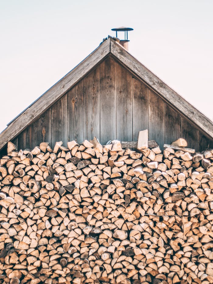 A rustic wooden shed with a neatly stacked pile of firewood against a clear sky.